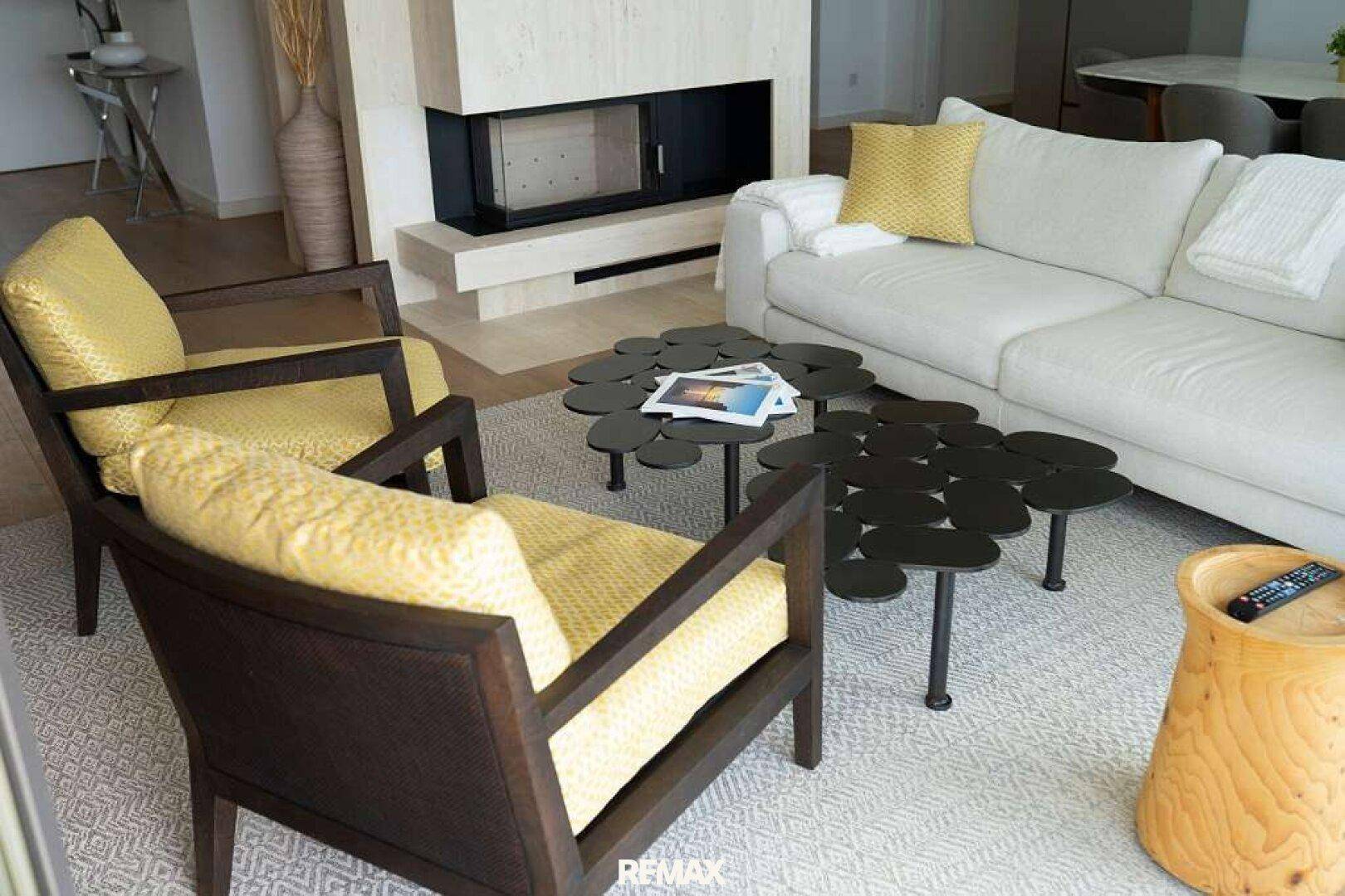 Helles Wohnzimmer mit modernem Kamin, weißem Sofa und zwei gelben Sesseln, ergänzt durch stilvolle Couchtische.