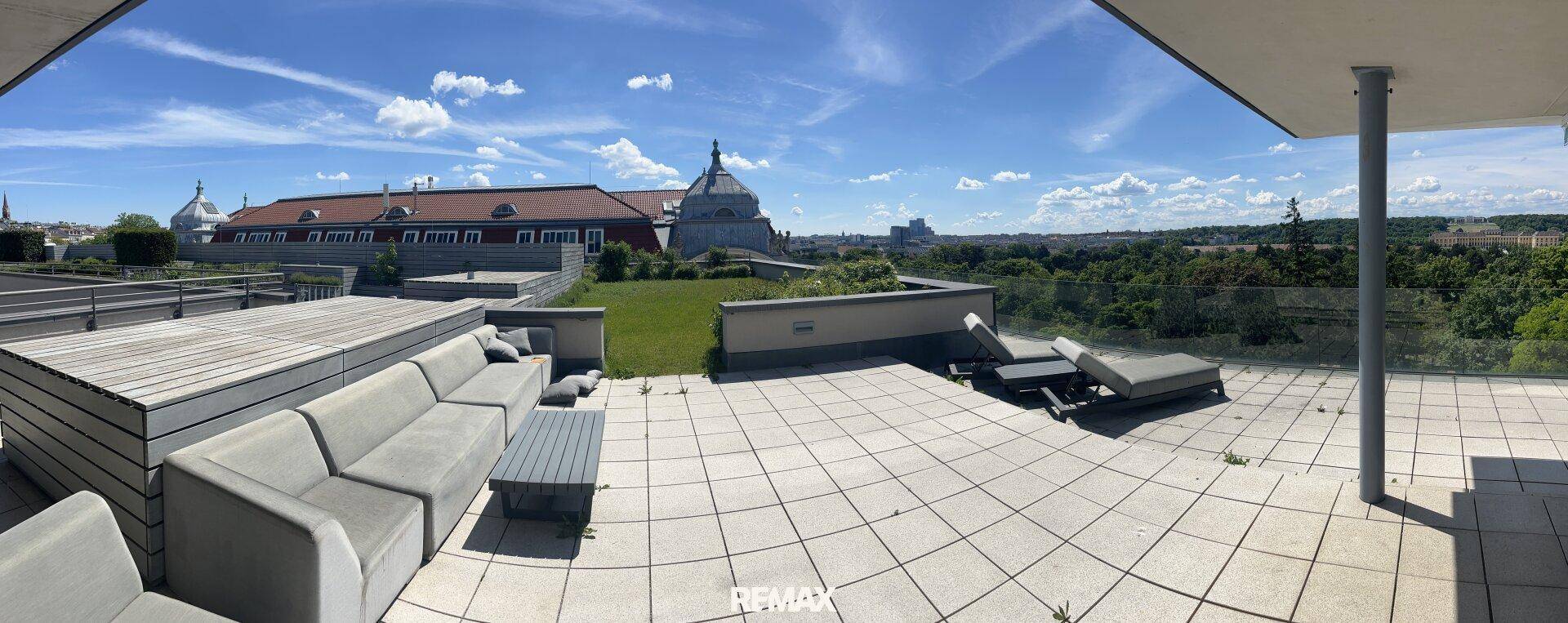 Panoramablick auf eine weitläufige Dachterrasse mit Lounge-Möbeln, Grünflächen und Stadtblick in der Ferne.