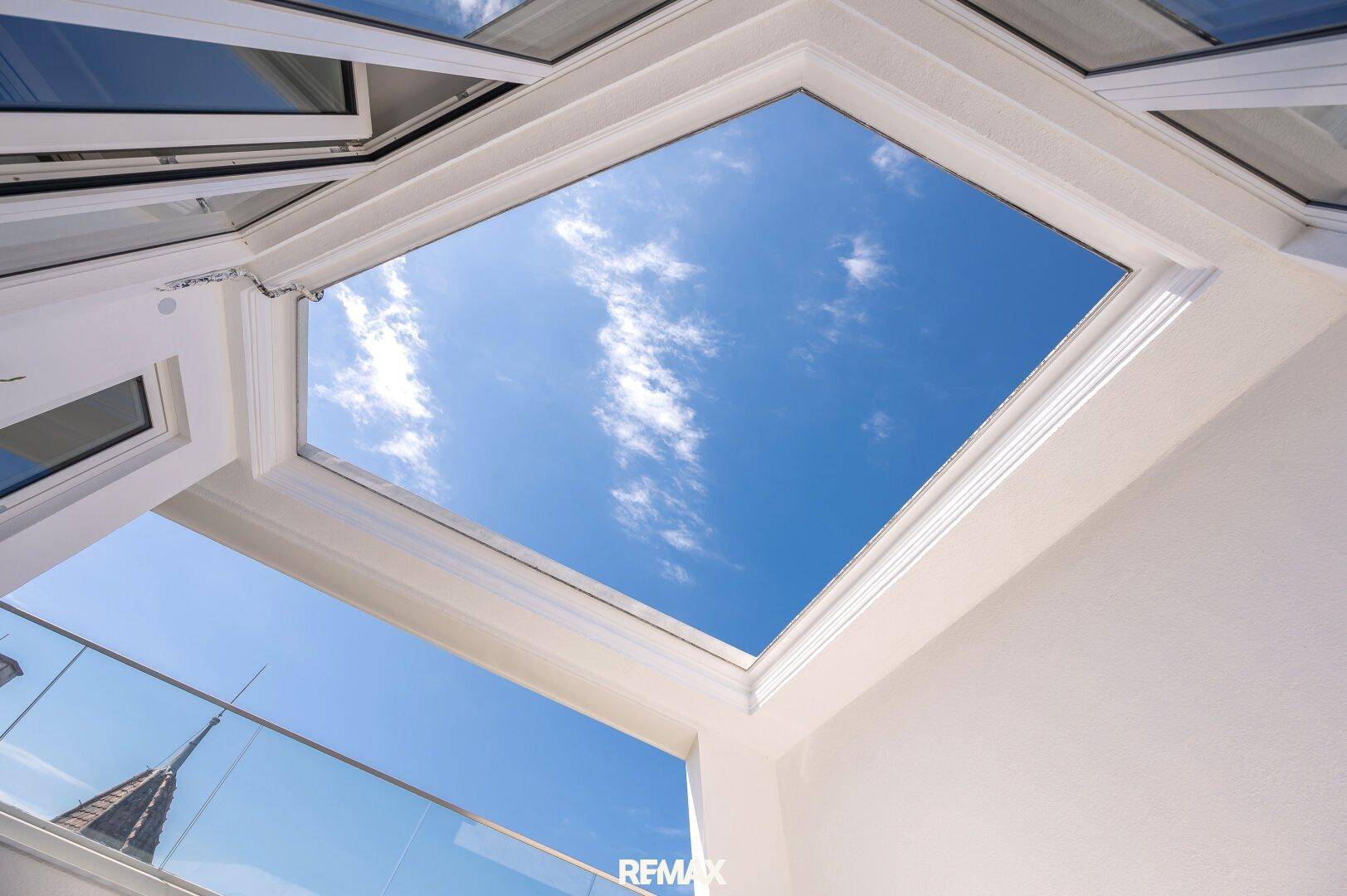 Offener Himmelsblick durch eine große Dachöffnung auf der sonnigen Terrasse.