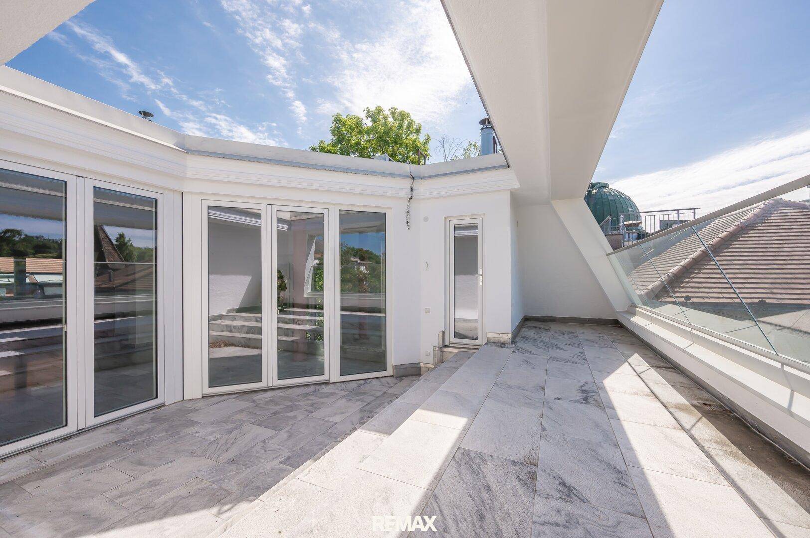 Helle Dachterrasse mit mehreren Zugängen zum Innenbereich und moderner Glasbrüstung.