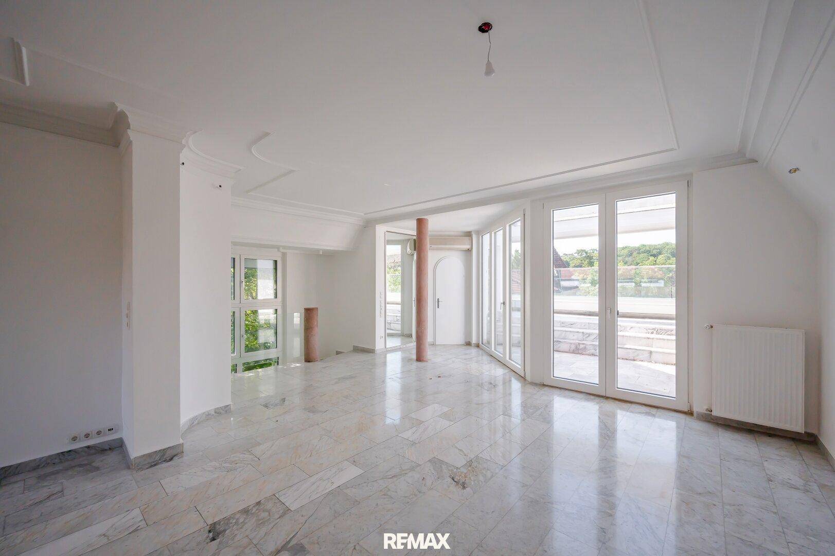 Großer, leerer Wohnraum mit eleganten Marmorfliesen und Zugang zur sonnigen Terrasse.