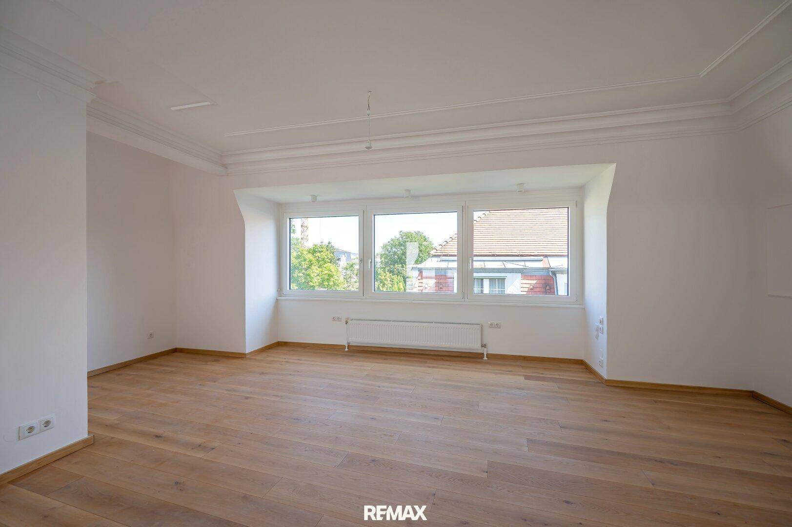 Geräumiges Zimmer mit hellem Holzboden und breiter Fensterfront für viel Tageslicht.