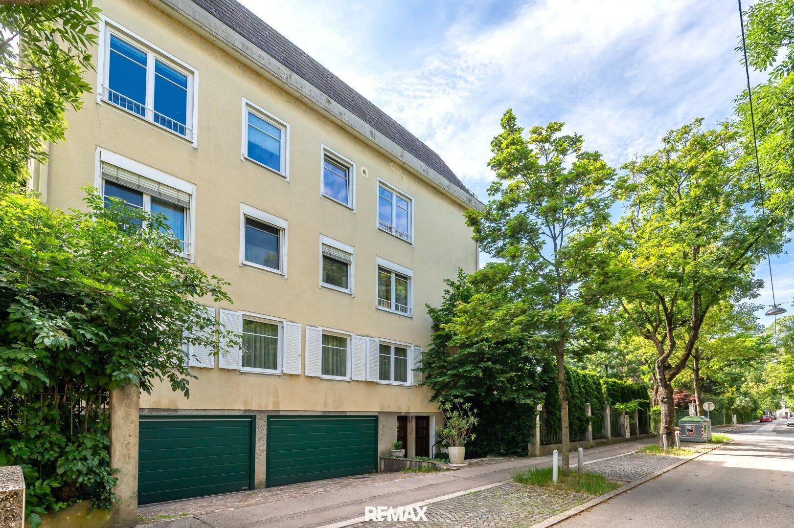 Mehrstöckiges Gebäude mit heller Fassade, grünen Garagentoren und üppiger Begrünung.