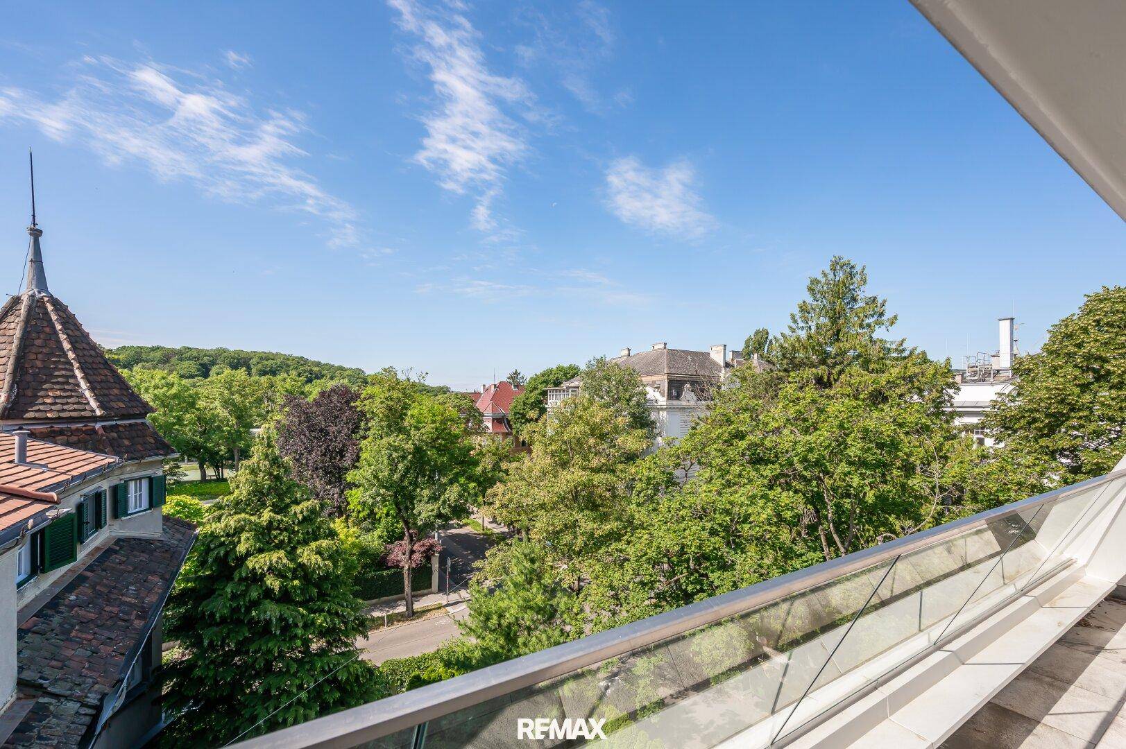 Panoramablick von der Terrasse auf eine grüne, baumreiche Umgebung mit historischer Architektur.