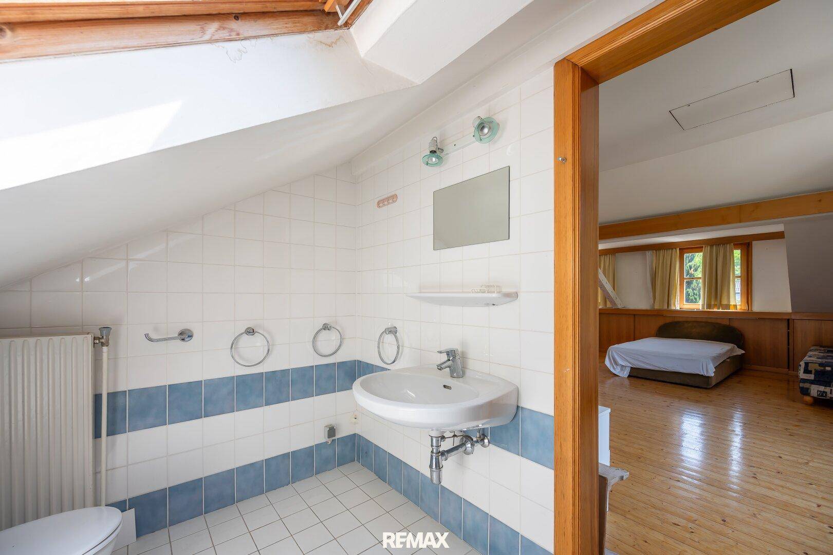 Badezimmer mit Waschbecken, Spiegel und Zugang zu einem angrenzenden Wohnbereich im Dachgeschoss.