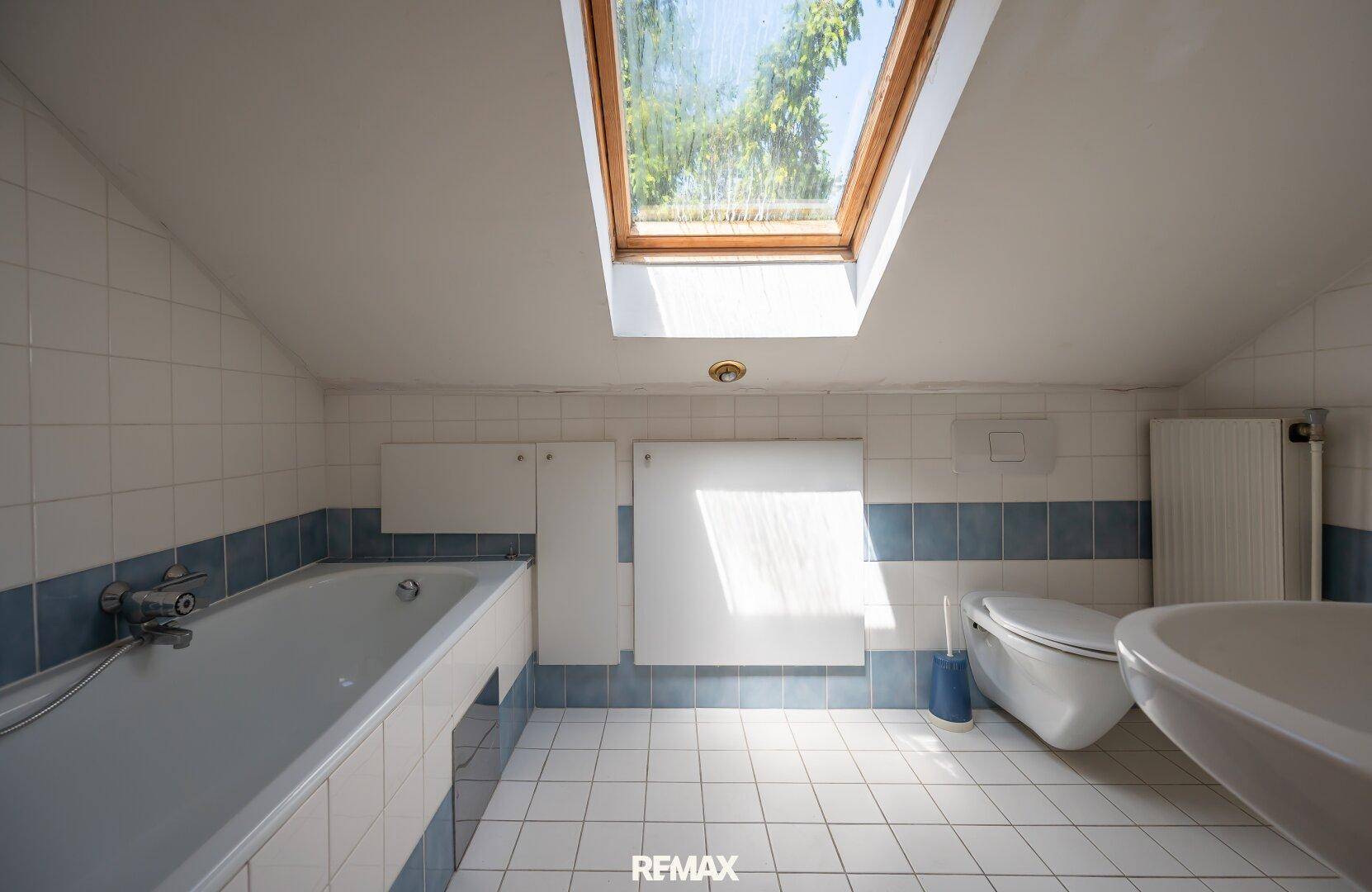 Helles Badezimmer im Dachgeschoss mit Badewanne, Fliesen und einem großen Dachfenster für natürliches Licht.
