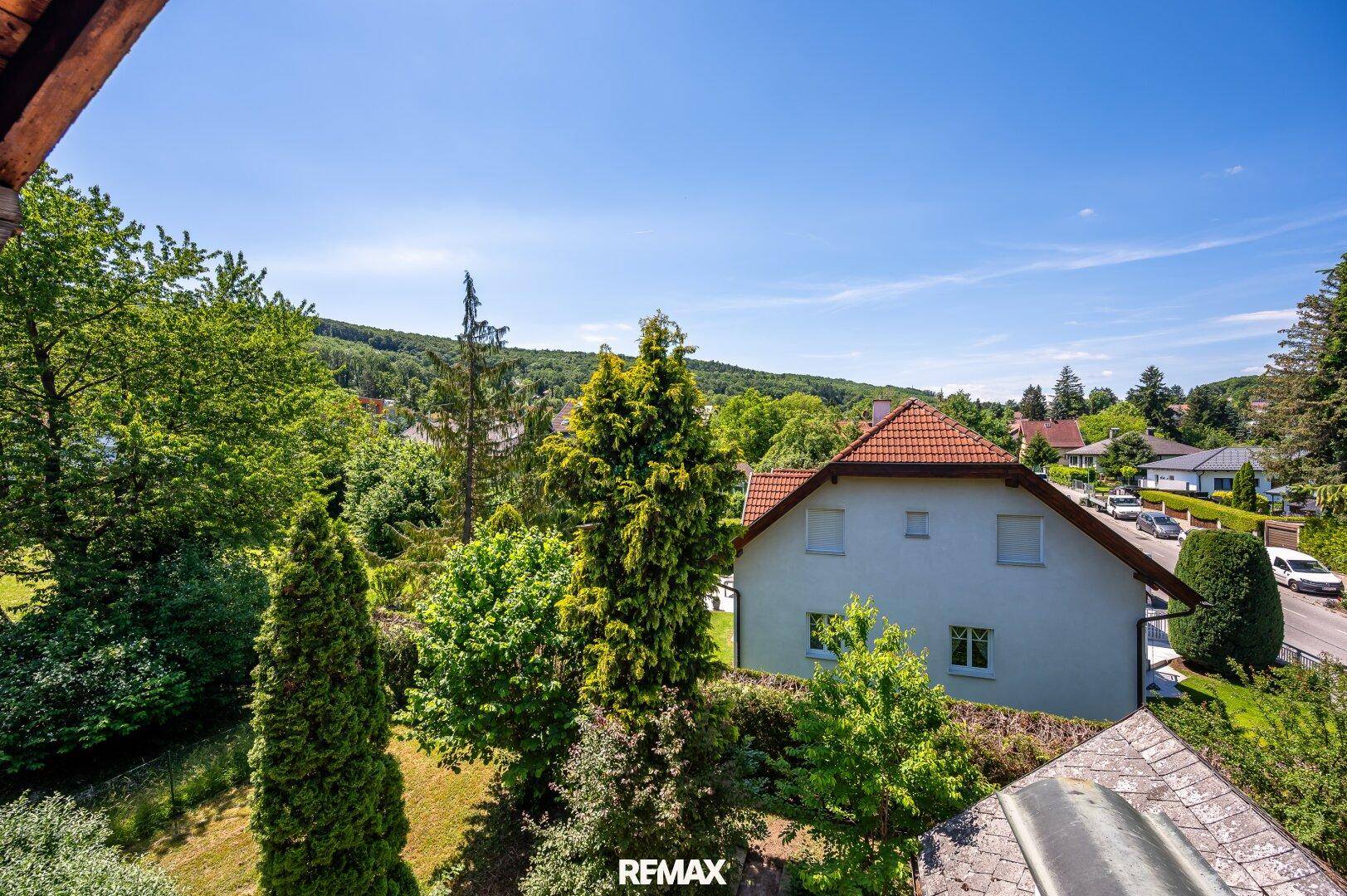 Weitläufiger Blick über die grüne Landschaft mit Wohnhäusern und viel Baumbestand an einem sonnigen Tag.
