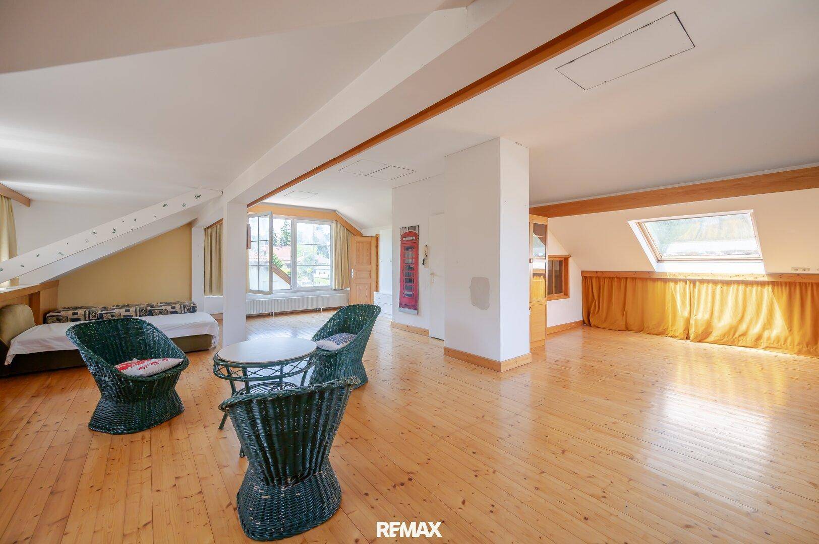 Helles, geräumiges Dachgeschosszimmer mit Holzboden, Schrägen und einem gemütlichen Sitzbereich.