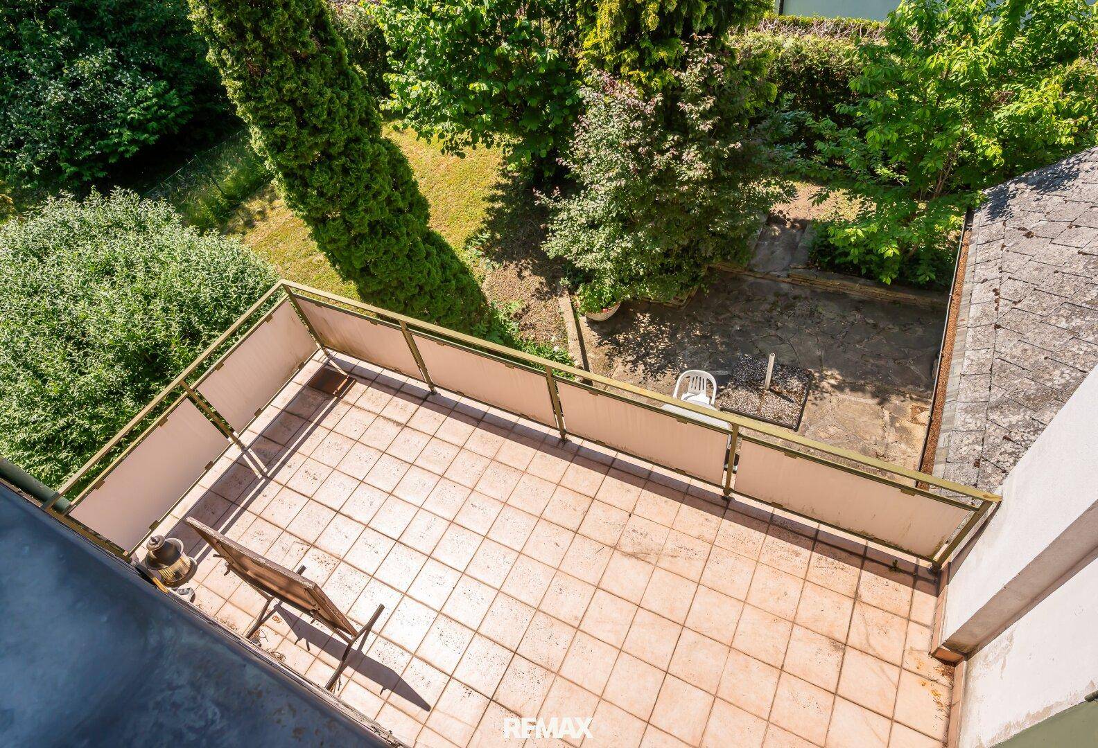 Blick von oben auf die geräumige, geflieste Terrasse mit einem Stuhl und Gartenblick.