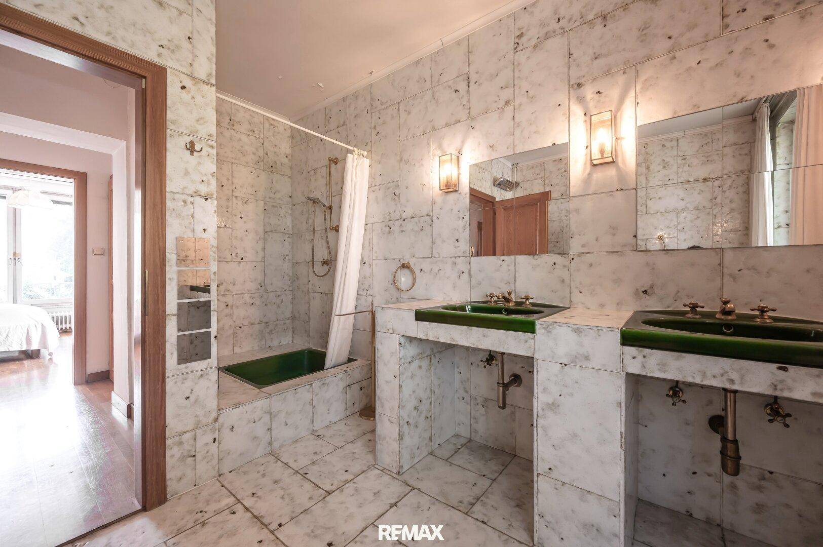 Großes Badezimmer mit Marmorfliesen, Doppelwaschbecken und Badewanne mit Duschvorhang.