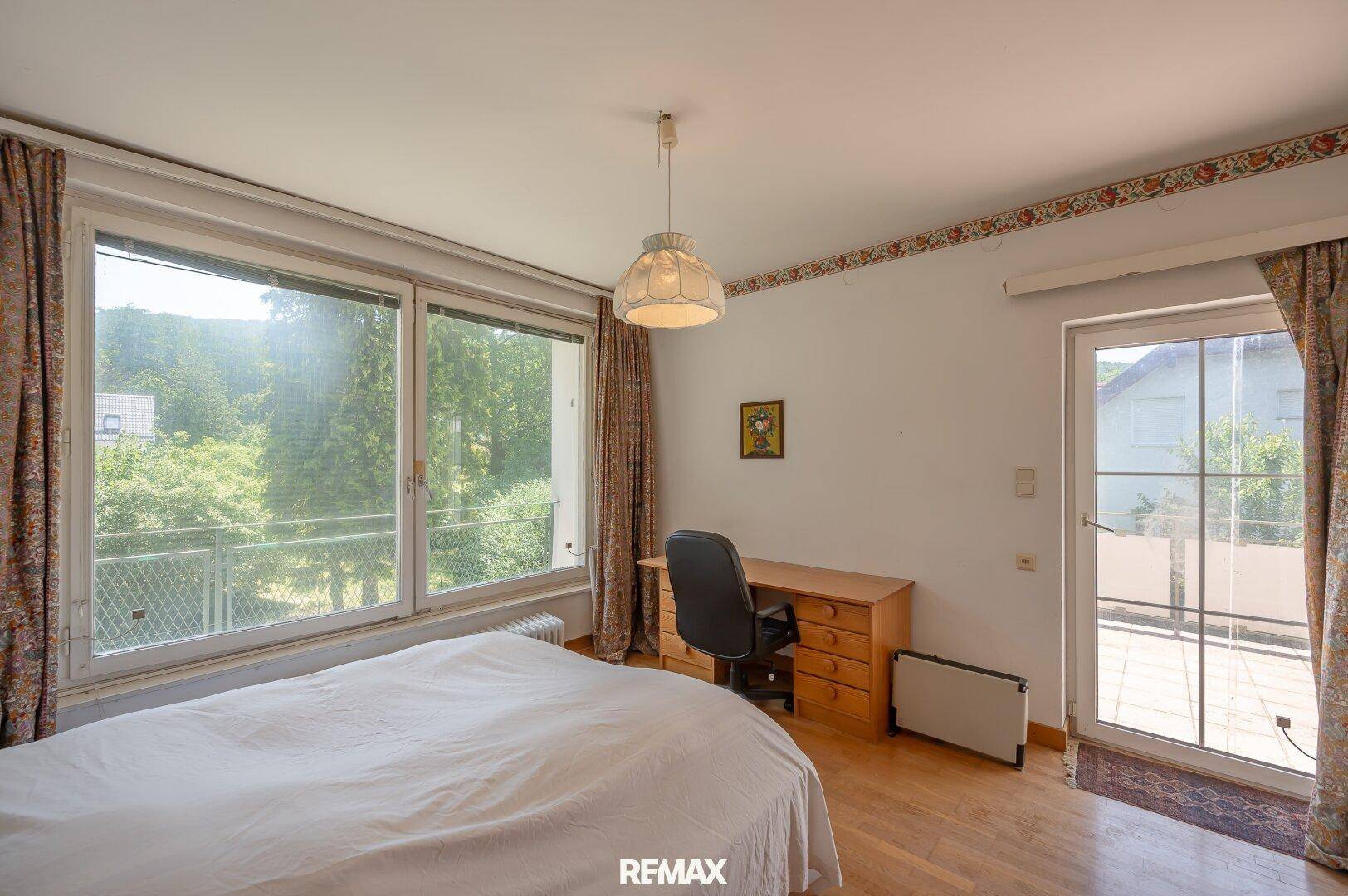Helles Zimmer mit Parkettboden, großem Fenster und Zugang zu einem weiteren Balkon.