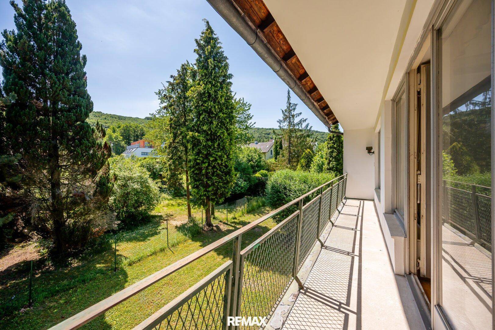 Langer Balkon mit Metallgeländer und weitem Blick über den grünen Garten und die Umgebung.