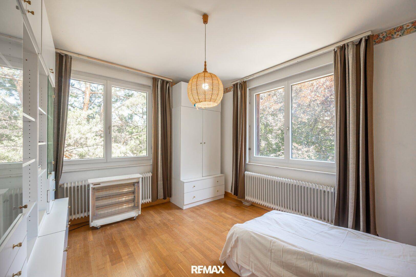 Helles Schlafzimmer mit Parkettboden, großen Fenstern und Blick ins Grüne.