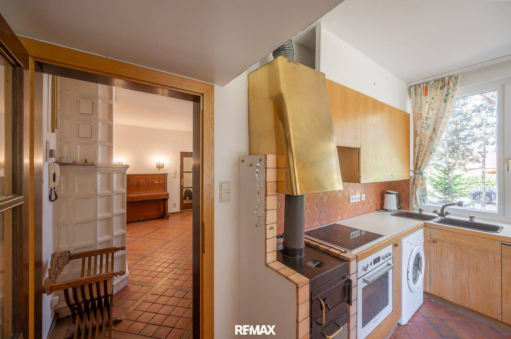Traditionelle Küche mit Holzelementen, Kachelofen und Blick auf den Flur mit Treppe.