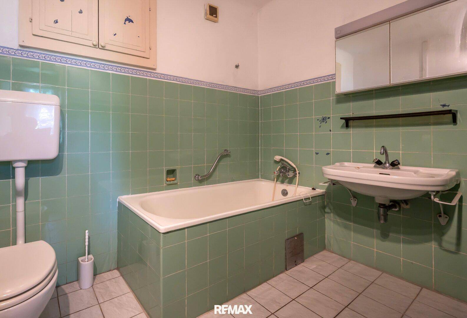 Badezimmer im Stil der 80er Jahre mit grünen Fliesen, Badewanne und Waschbecken.