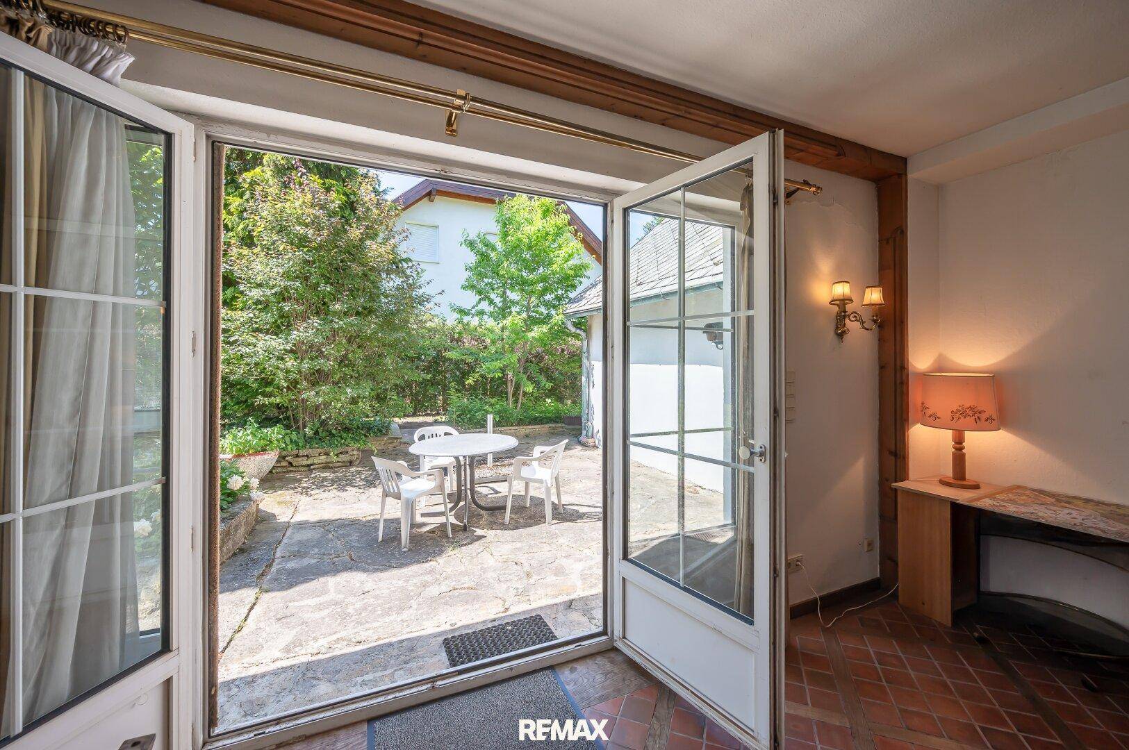 Heller Raum mit direktem Zugang zu einer gepflasterten Terrasse mit Gartenmöbeln im Grünen.