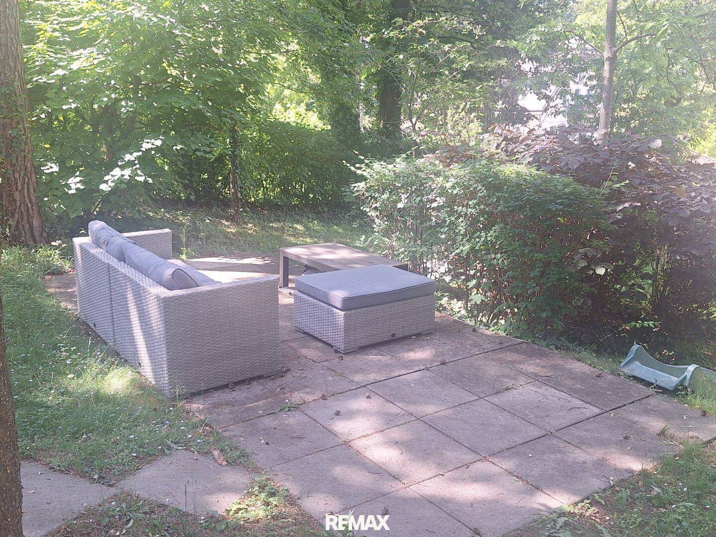 Gemütlicher Sitzbereich im Freien auf einer gepflasterten Terrasse, umgeben von üppigem Grün.