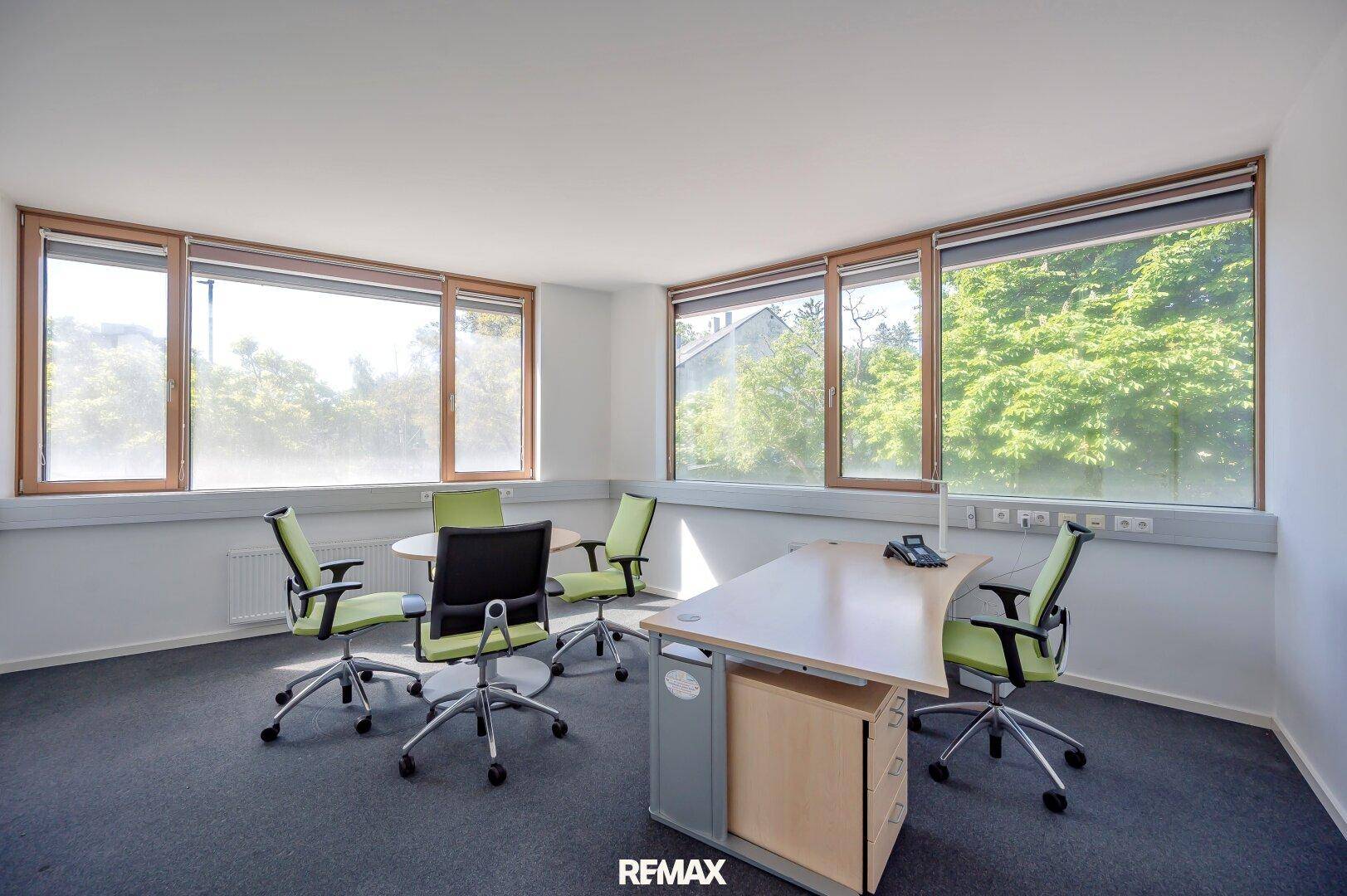 Helles Büro oder Besprechungsraum mit runden Tisch und grünen Bürostühlen.