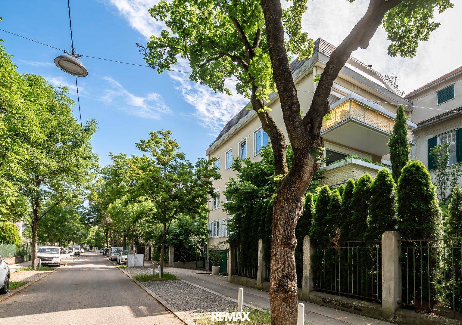 Ansicht des Gebäudes von der Straße, umgeben von Bäumen und einer ruhigen Wohngegend.