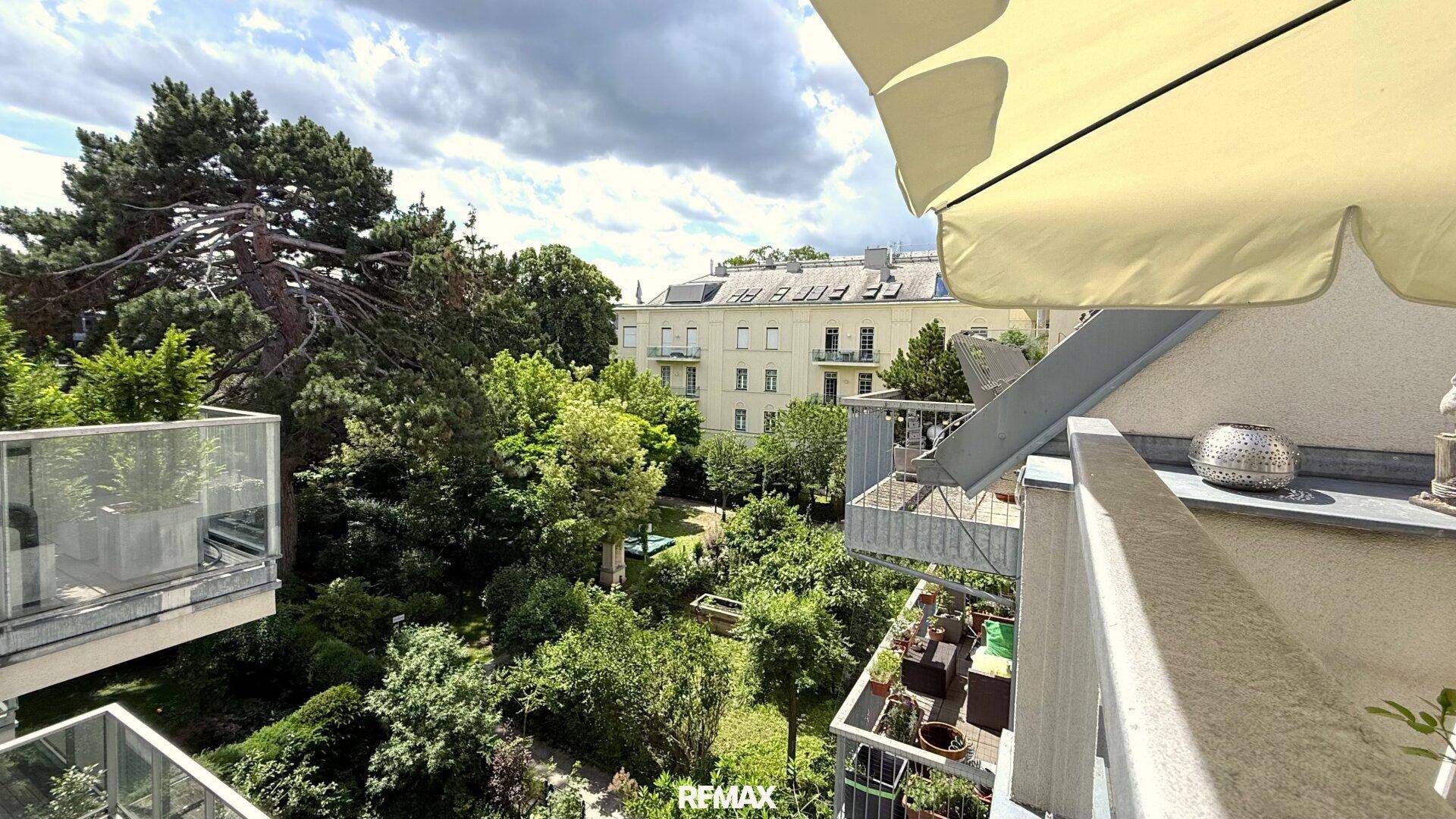 Balkon mit Blick auf einen grünen Innenhof und umliegende Gebäude unter bewölktem Himmel.