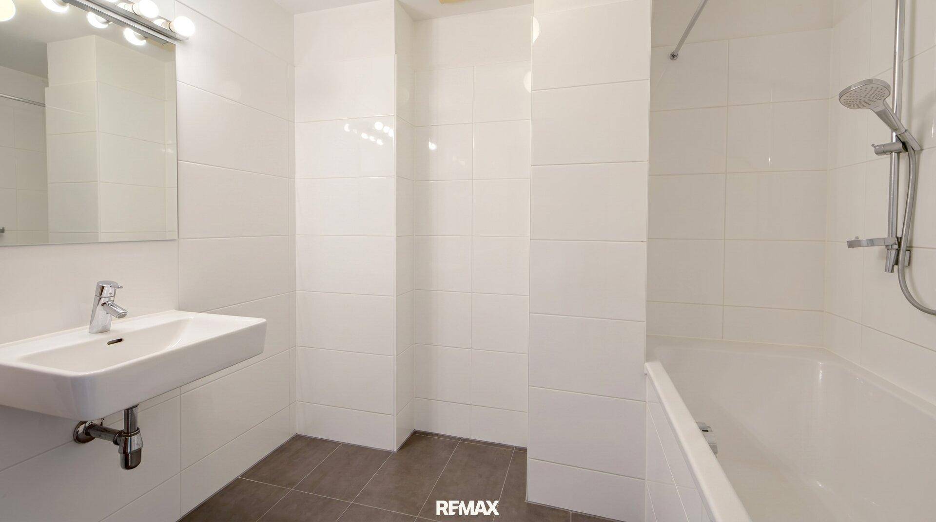 Modernes Badezimmer mit weißen Fliesen, einem schwebenden Waschbecken und einer Badewanne.
