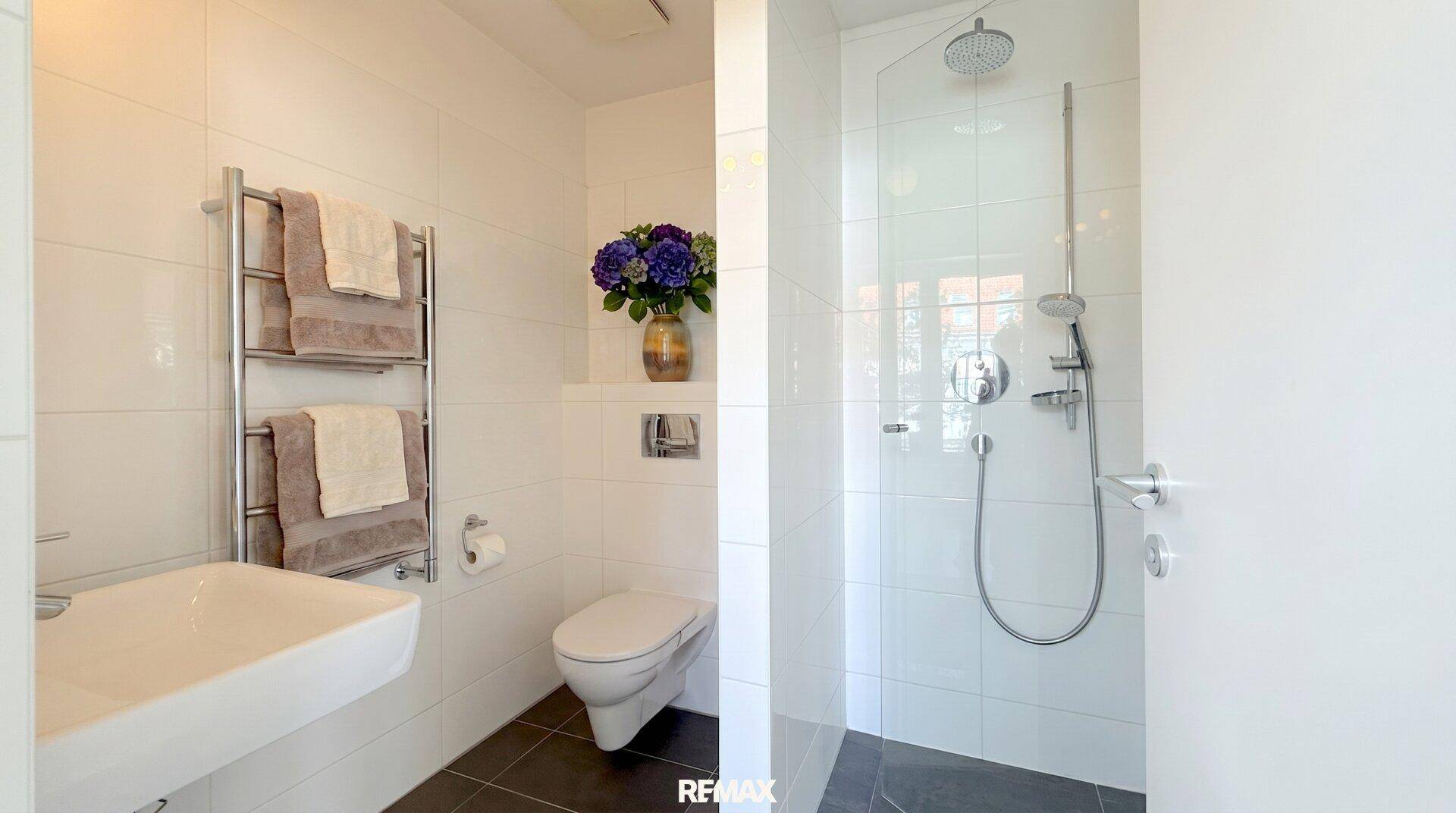 Modernes Badezimmer mit weiß gefliesten Wänden, begehbarer Dusche und beheiztem Handtuchhalter.