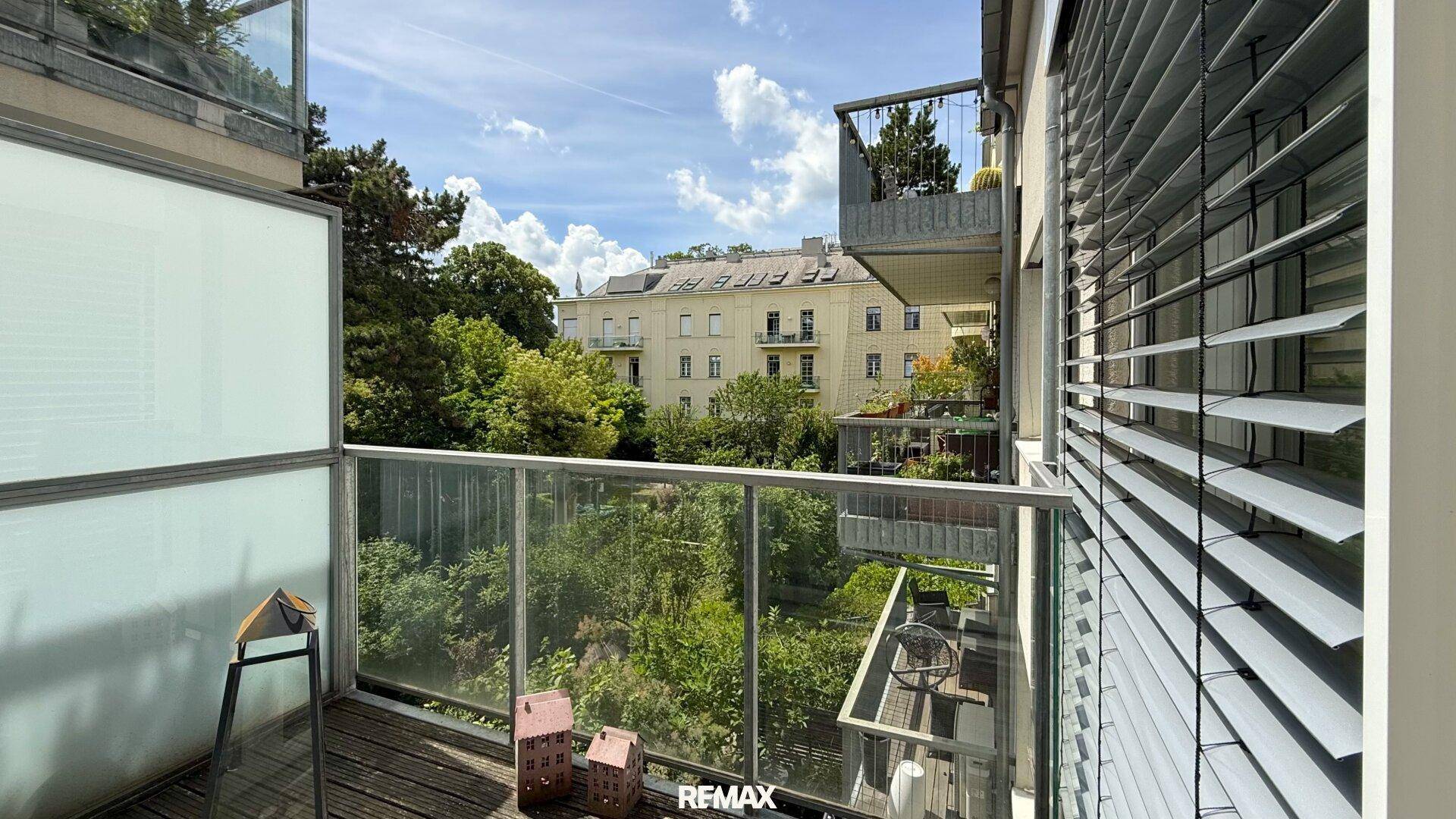 Balkon mit Glasgeländer und einem schönen Blick auf grüne Bäume und umliegende Gebäude.