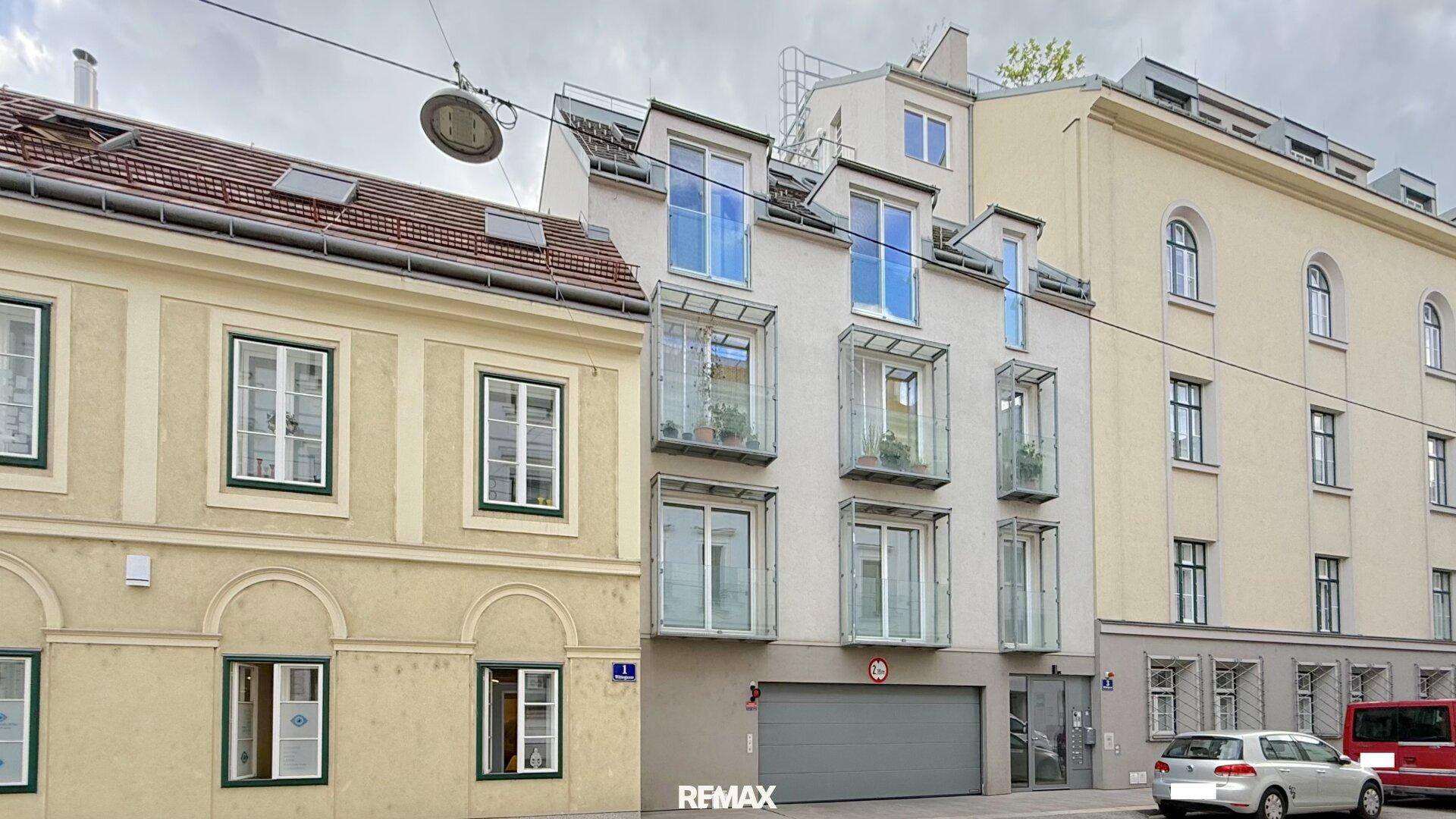 Fassade eines modernen Wohngebäudes mit Balkonen und angrenzenden Altbauten in einer städtischen Umgebung.