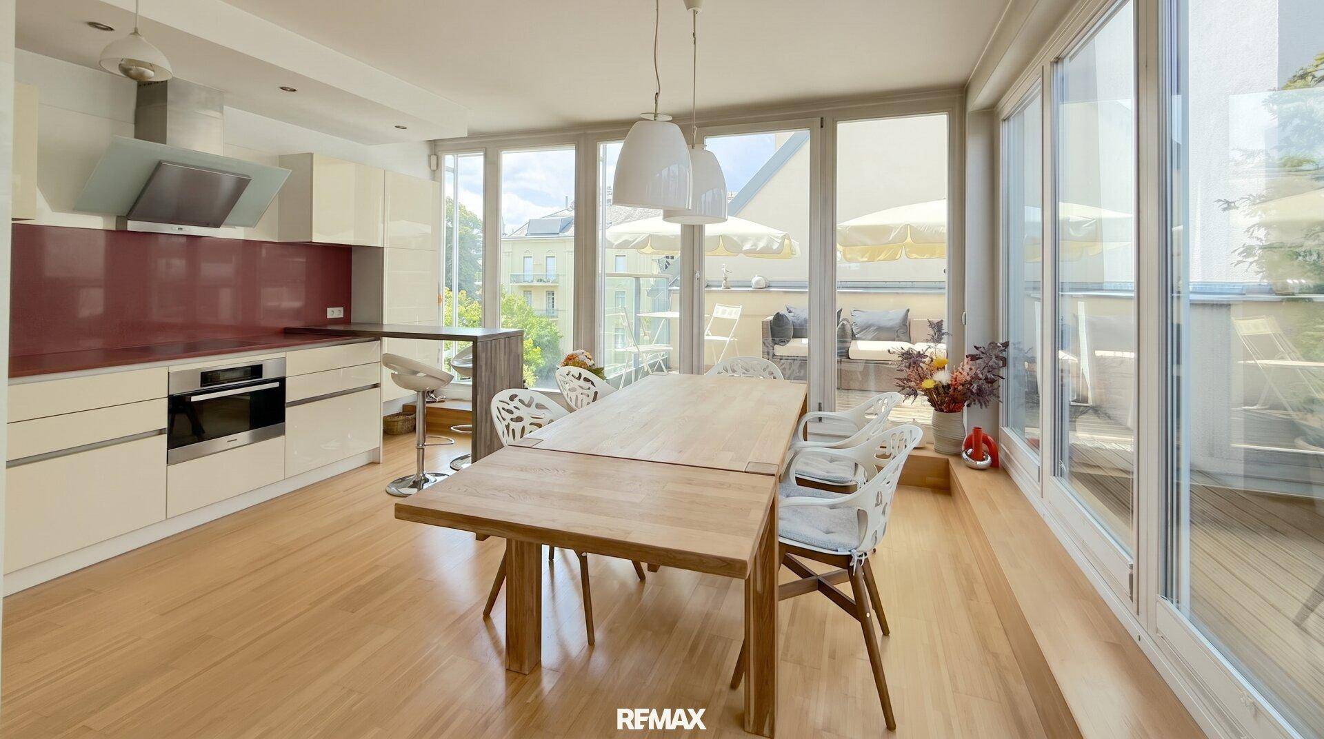 Moderne offene Küche mit Essbereich, hellen Schränken und Zugang zu einer sonnigen Terrasse.