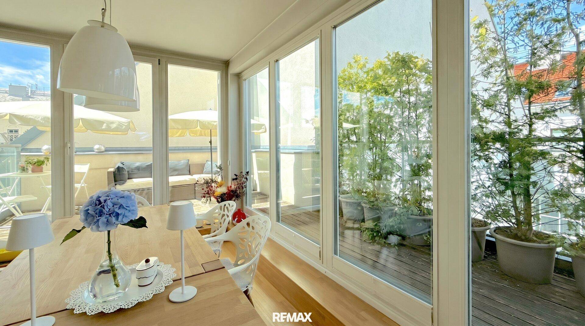 Heller Essbereich mit Holztisch und großen Fenstern, die viel Tageslicht hereinlassen und Blick auf die Terrasse bieten.