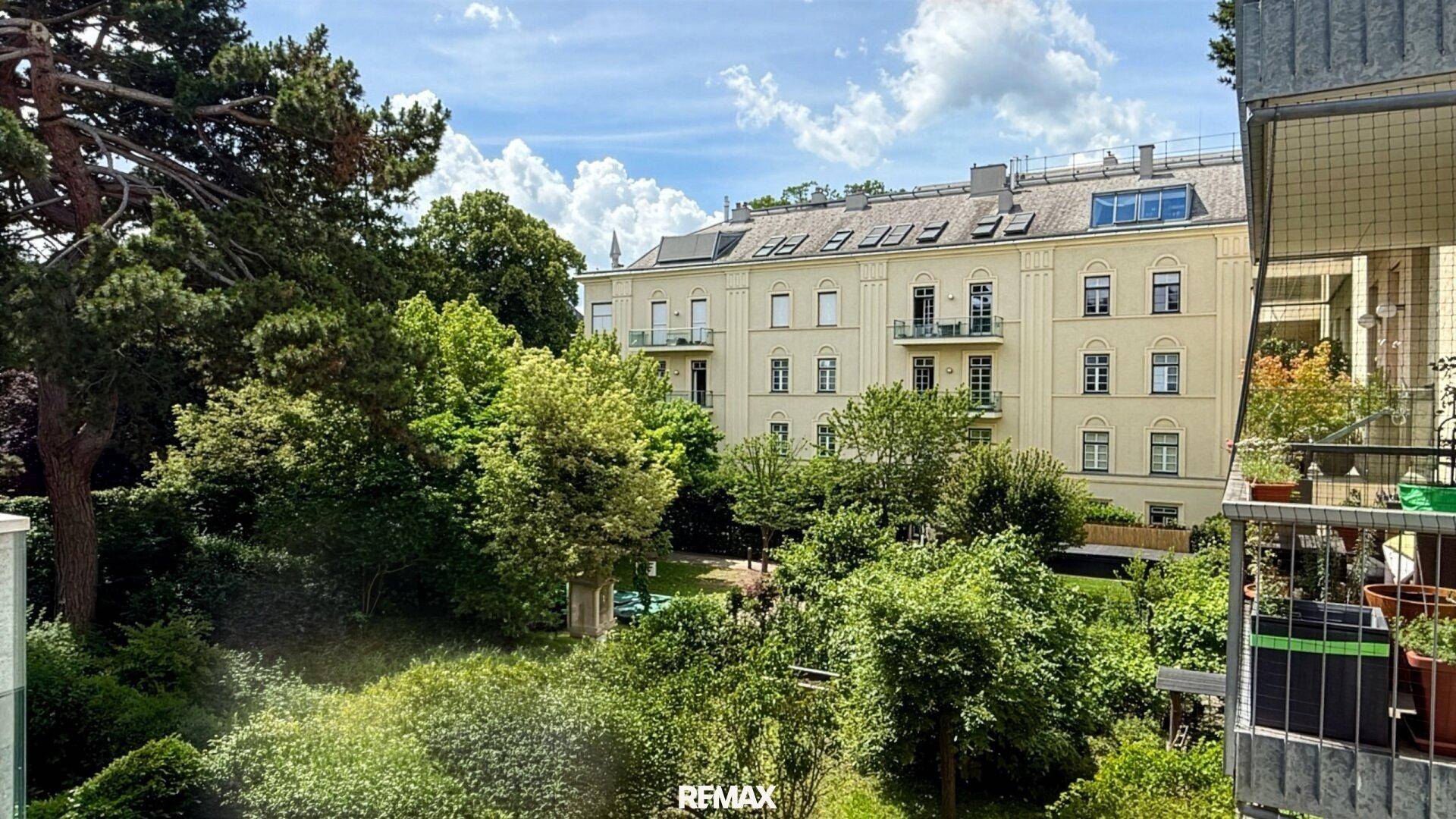 Weitläufiger Blick ins Grüne mit altem Baumbestand und einem historischen Gebäude im Hintergrund.