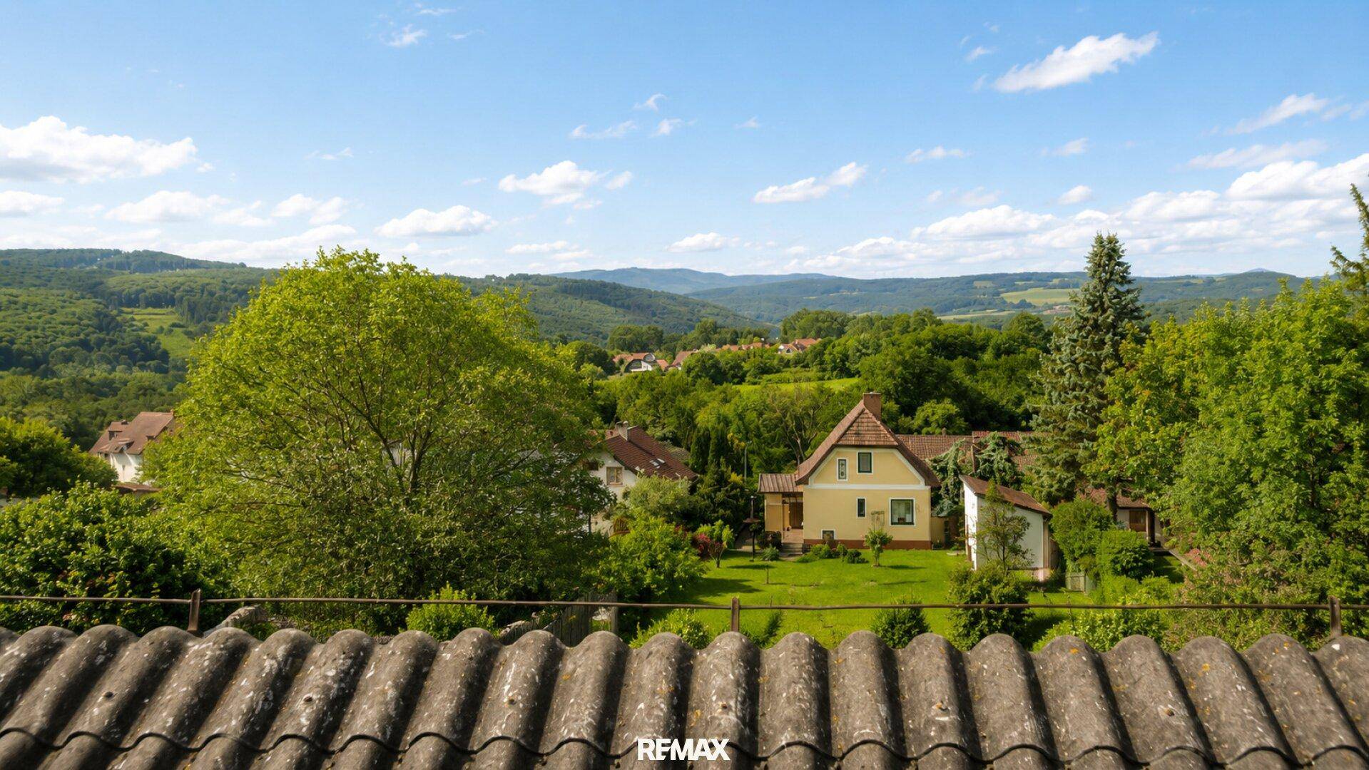 Panoramablick über Dächer und grüne Hügel, mit weiteren Häusern in der Ferne.