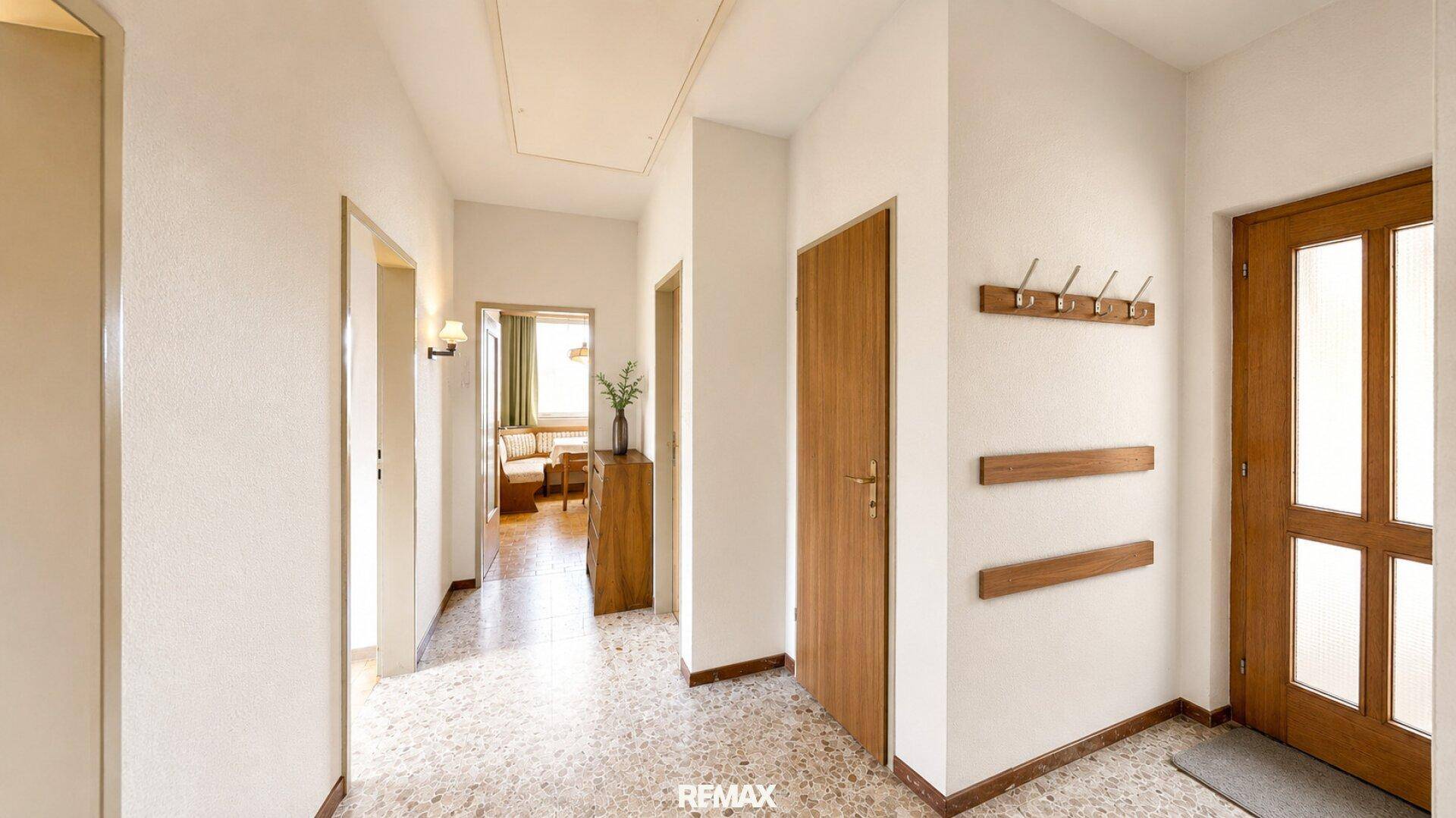 Heller Flur mit Terrazzoboden, Holztüren und Garderobe, der zu weiteren Räumen führt.
