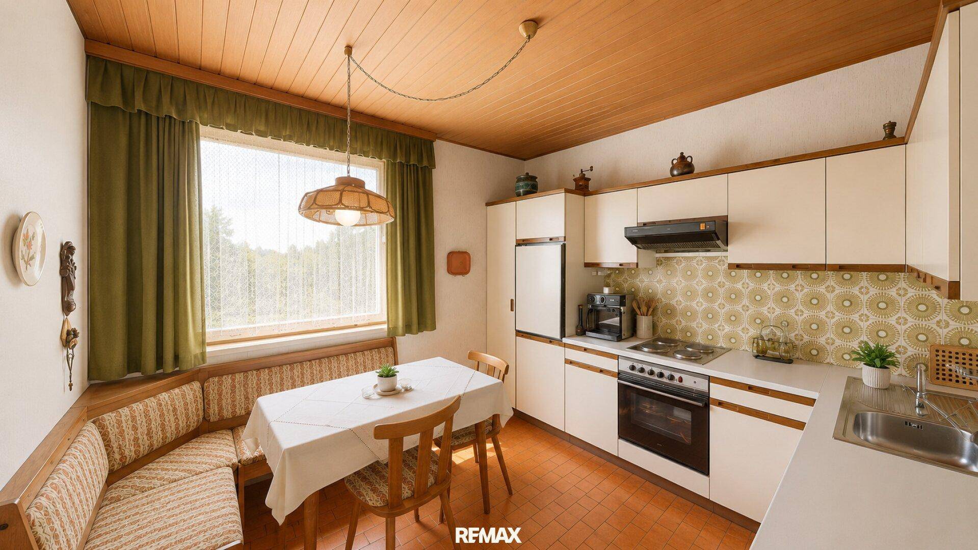 Traditionelle Wohnküche mit Einbauküche, Essbereich und Holzdecke, hell durch großes Fenster.