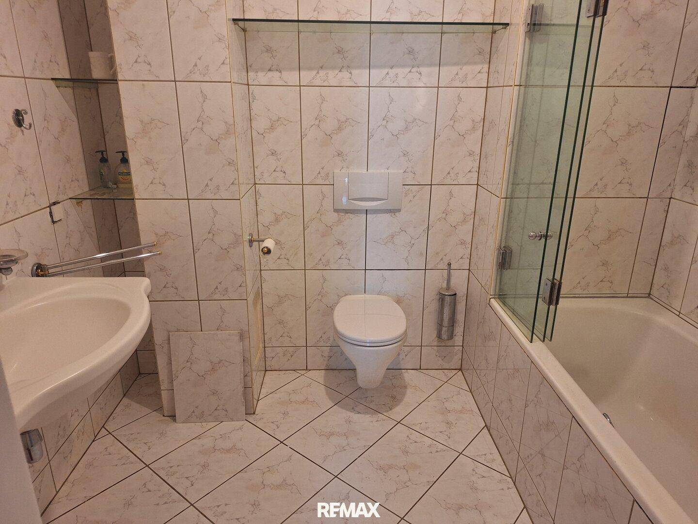Gefliestes Badezimmer mit Badewanne, WC, Waschbecken und einer modernen Glasduschwand.