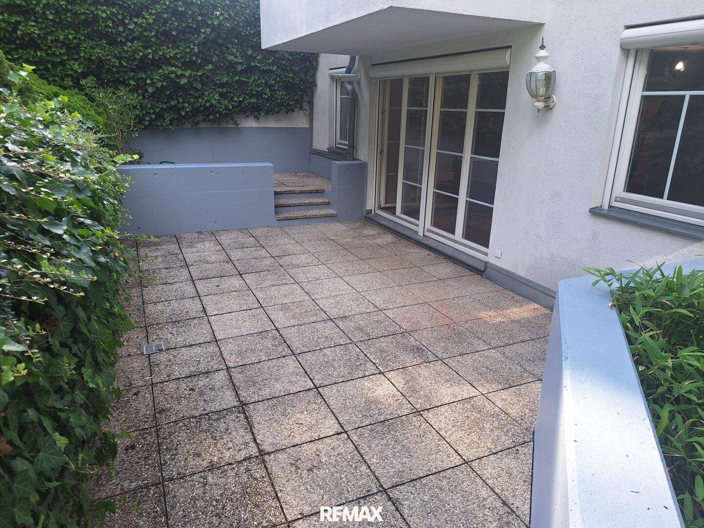 Geräumige, gepflasterte Terrasse am Haus mit Zugang zu einem erhöhten Gartenbereich.