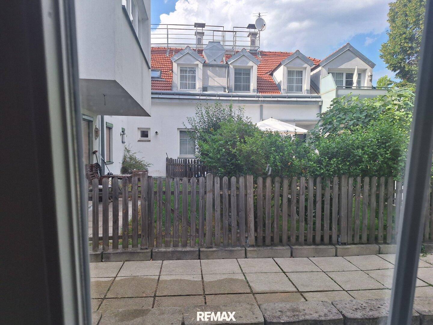 Blick aus dem Fenster auf einen kleinen, eingezäunten Gartenbereich und die Rückseite des Gebäudes.