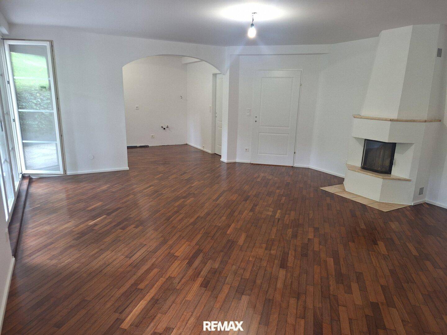 Helles Wohnzimmer mit Parkettboden, Kamin und Zugang zu einer Terrasse durch große Glastüren.
