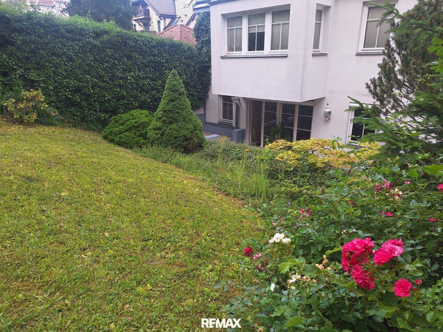 Detailansicht des Gartens mit blühenden Rosenbüschen und einer gepflegten Hecke vor der Hausfassade.