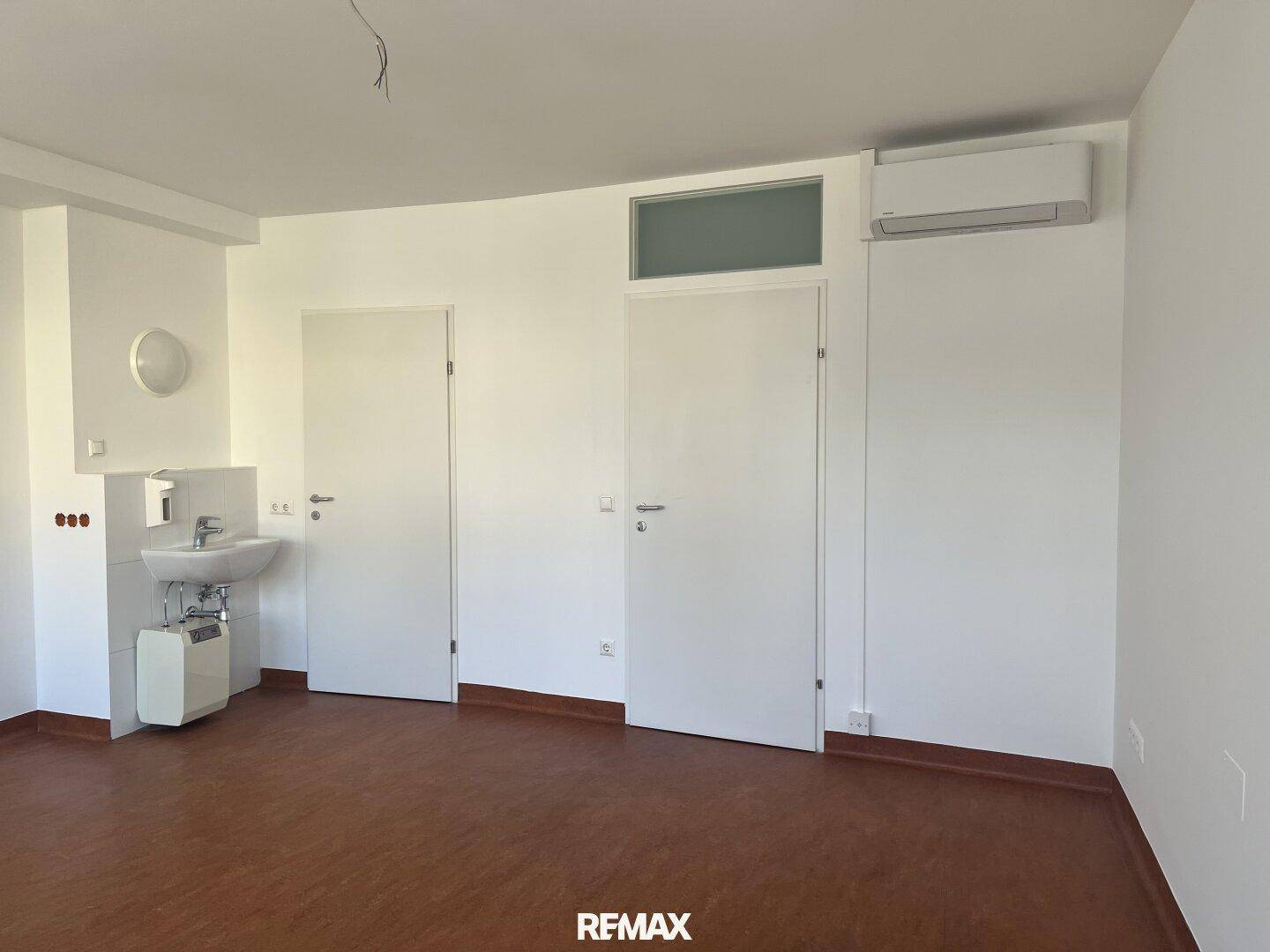 Heller Raum mit Waschbecken, Klimaanlage und zwei Türen, ideal für gewerbliche Nutzung oder als Büro.