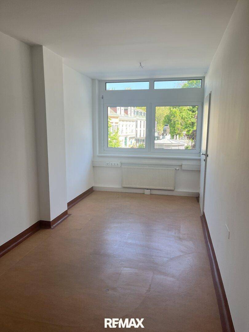 Heller Raum mit großen Fenstern, hellem Holzfußboden und einem Heizkörper, bietet viel Tageslicht.
