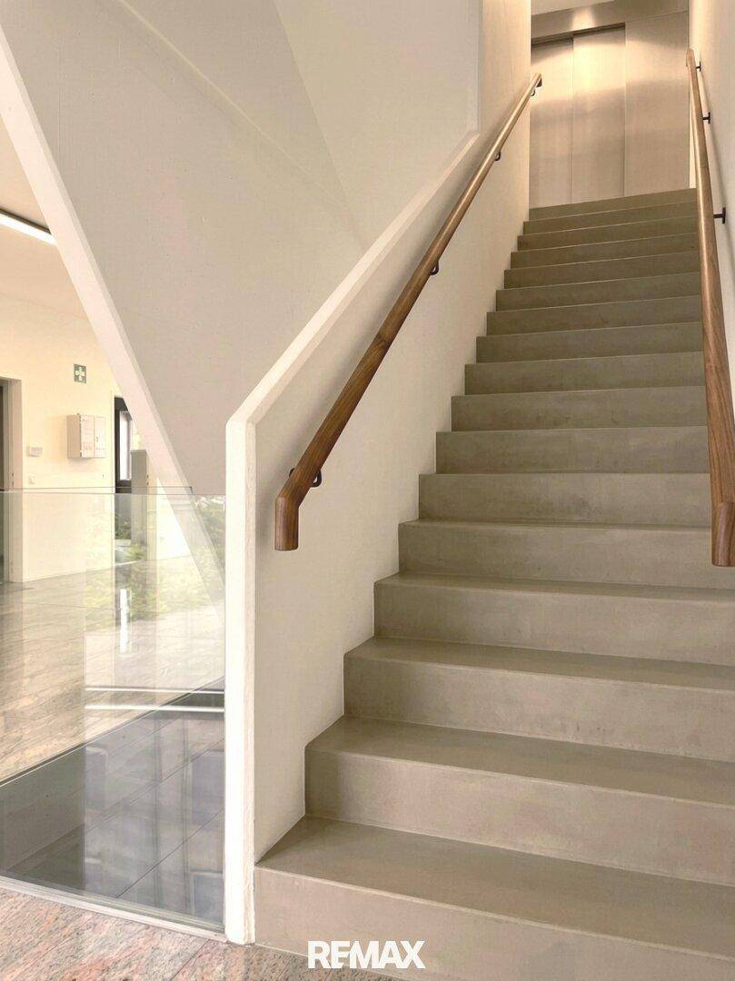 Moderne Treppe mit Holzhandlauf und glatten Stufen, führt zu oberen Etagen.