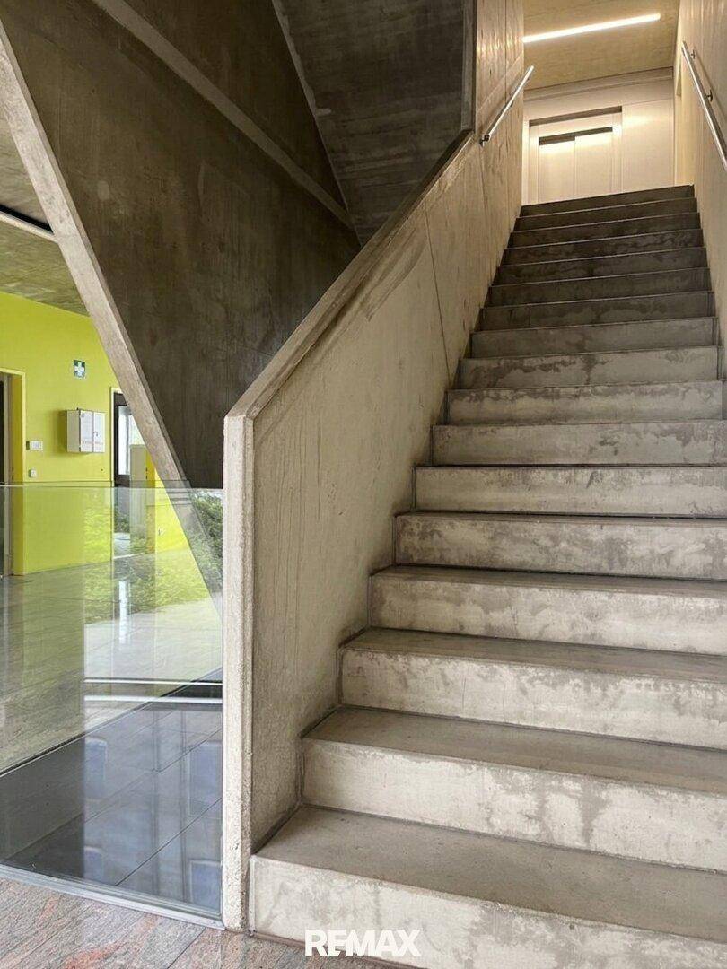 Treppenhaus mit Sichtbetonwänden und -stufen, daneben ein Aufzug.