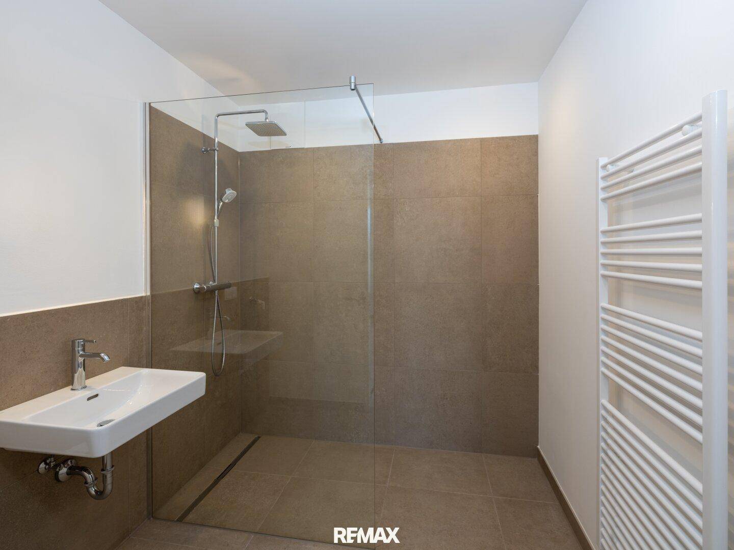 Modernes Badezimmer mit ebenerdiger Dusche, Einzelwaschbecken und beheiztem Handtuchhalter.
