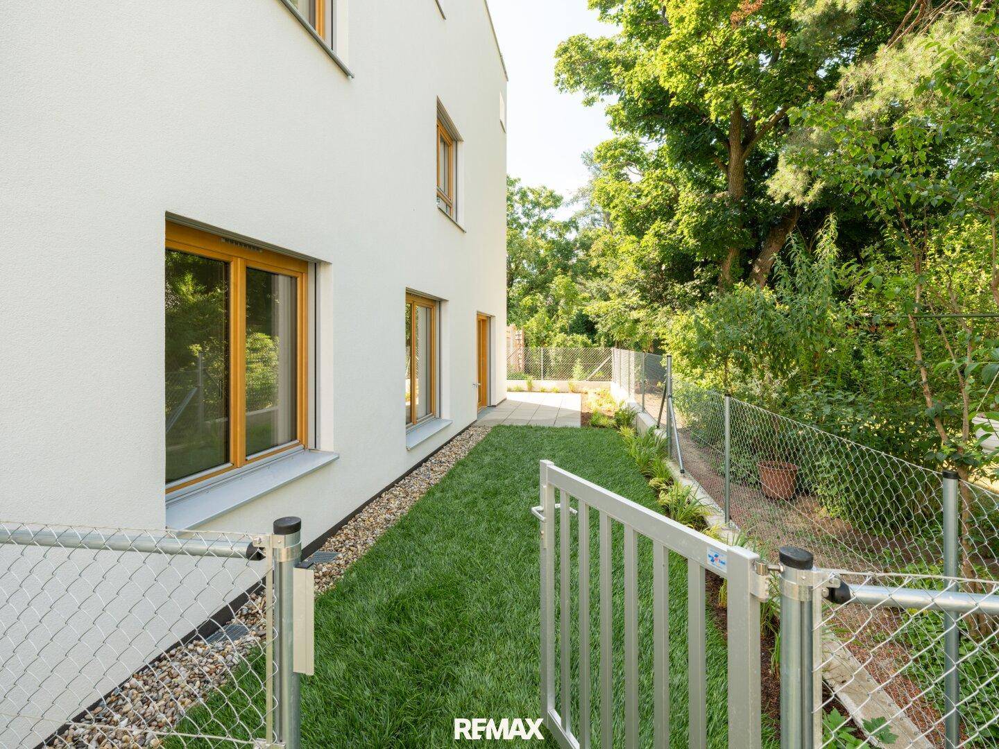 Kleiner, eingezäunter Gartenbereich neben dem Gebäude mit Rasenfläche und umgebenden Bäumen.
