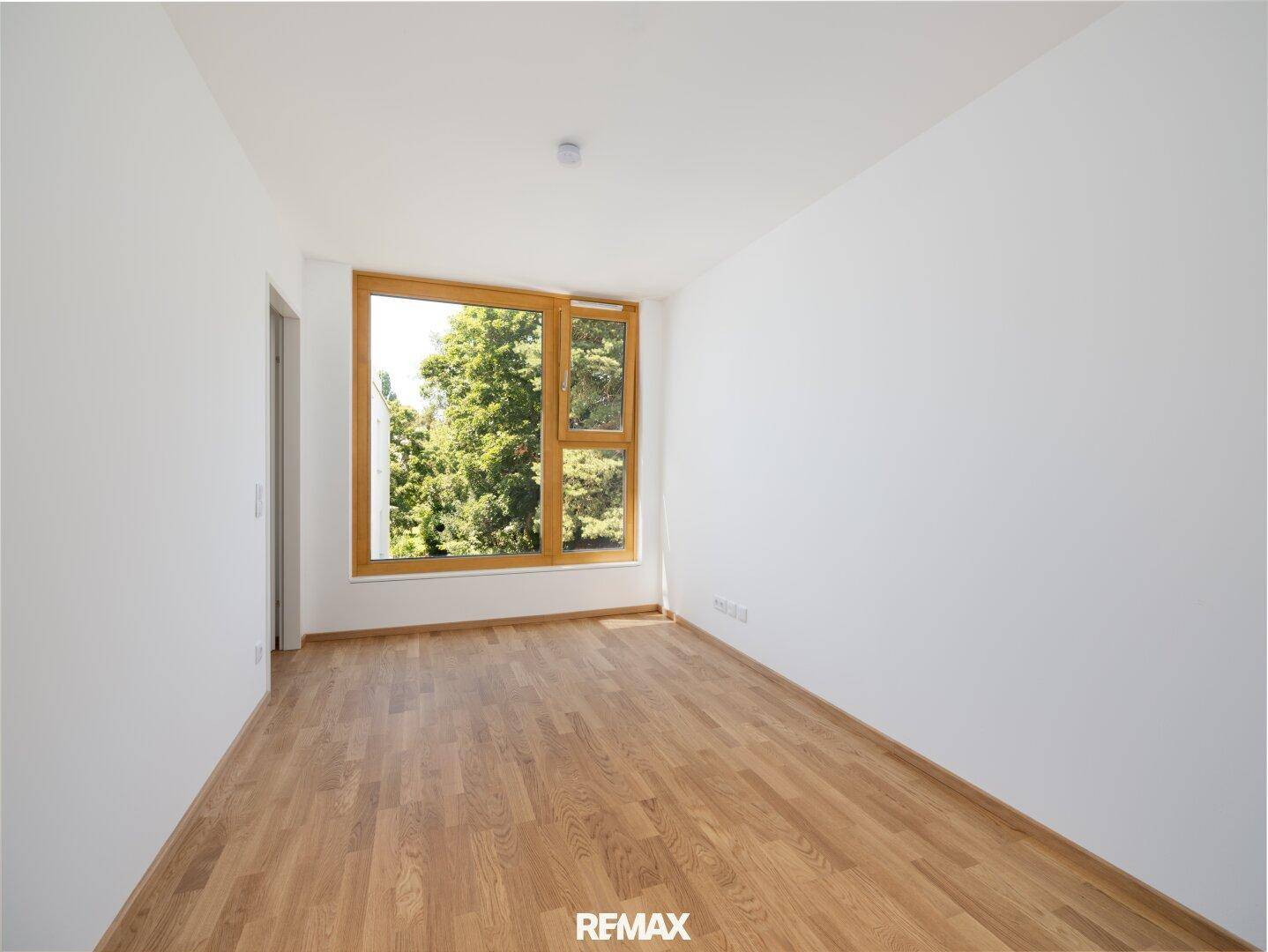 Leeres Schlafzimmer mit Holzboden und großem Fenster, das einen schönen Blick ins Grüne bietet.