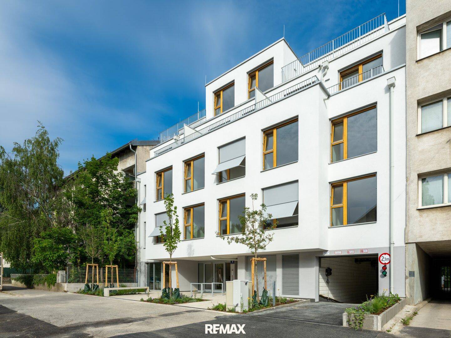 Seitenansicht eines modernen weißen Gebäudes mit Tiefgaragenzufahrt und großen Fenstern.