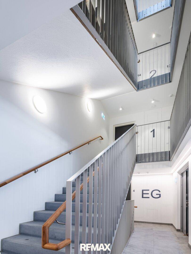 Modernes Treppenhaus mit grauen Stufen, Metallgeländer und Holzhandlauf in einem Mehrfamilienhaus.