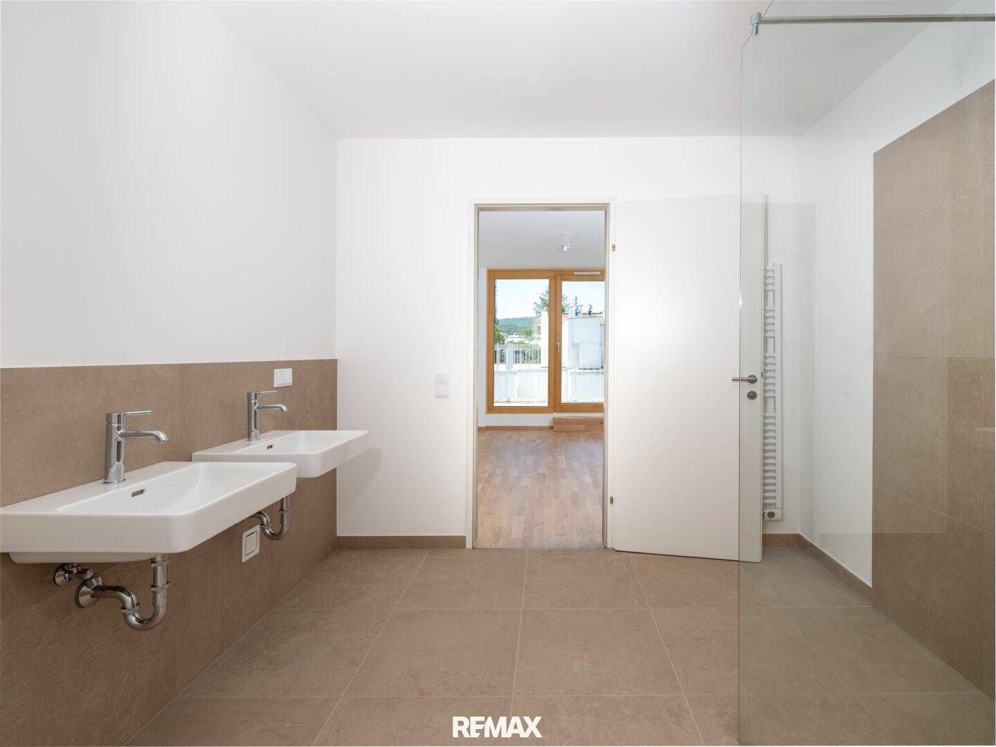 Modernes Badezimmer mit Doppelwaschbecken, ebenerdiger Dusche und hellen Fliesen.