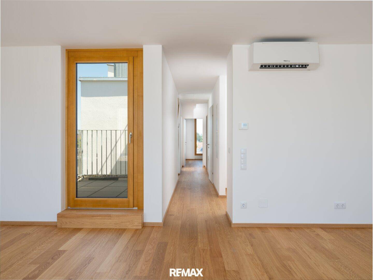 Heller Flur mit Holzboden, Klimaanlage und Zugang zu einem französischen Balkon.